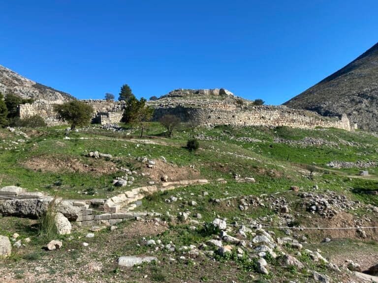 Ancient ruins on a hillside with stone structures and greenery under a clear blue sky.