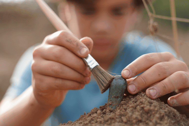 Young boy planting a sapling with a small shovel outdoors.