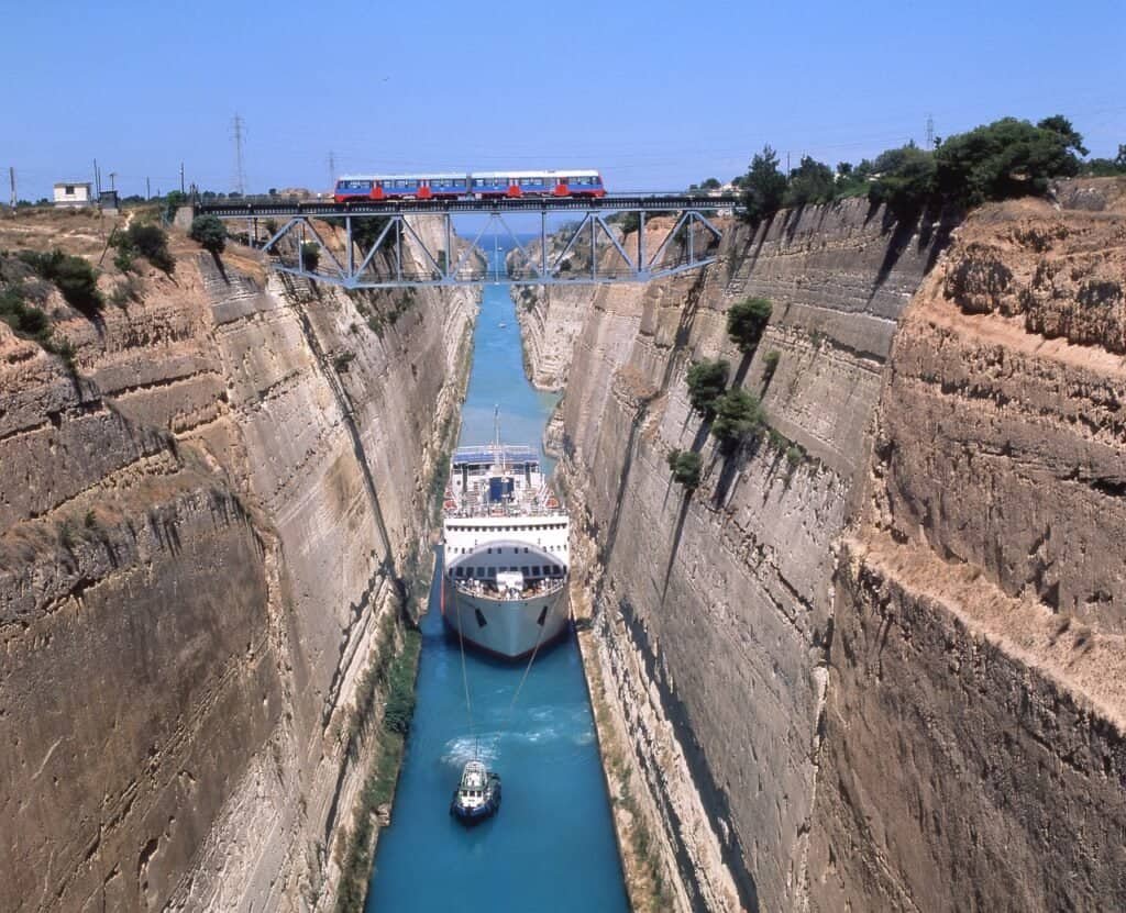 Scenic view of a canal with a cruise ship passing through, train crossing a bridge above.