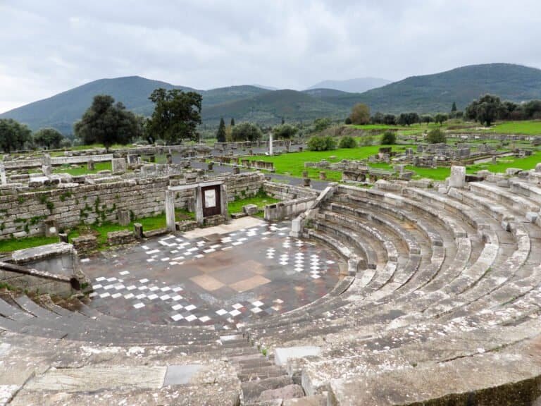 Ruins of an ancient Greek theater with stone seating and scenic mountain backdrop.