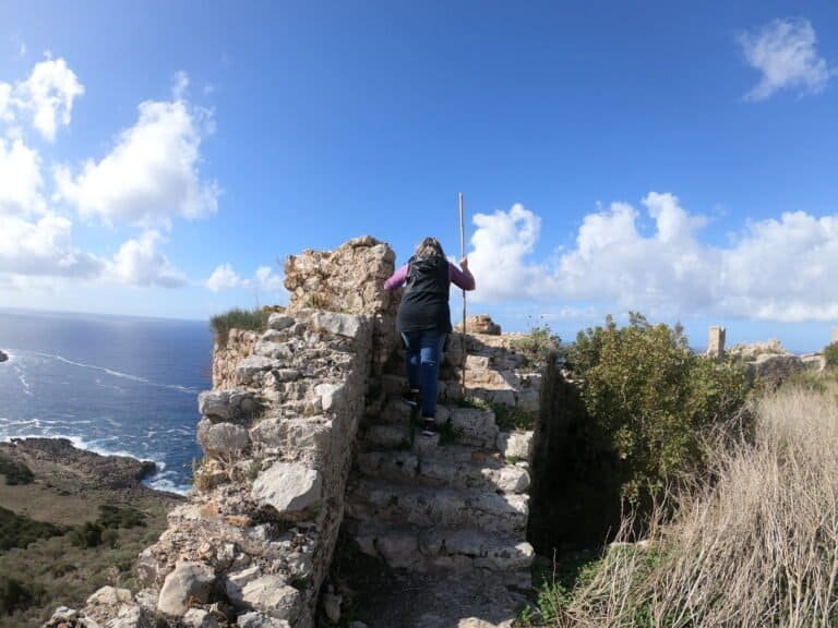 Person climbing ancient stone stairs overlooking the sea.