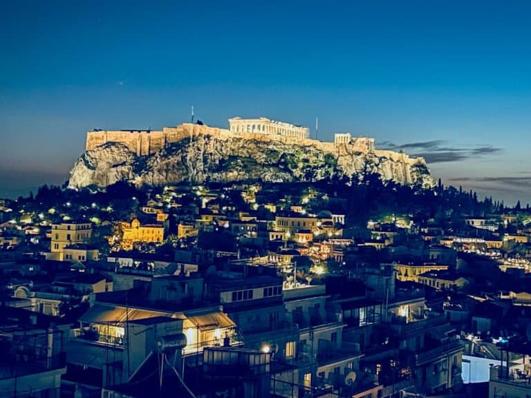 Acropolis of Athens illuminated at dusk, showcasing historic ruins and cityscape.
