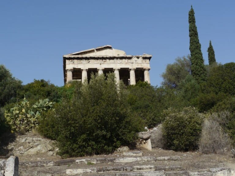 Historic Greek temple surrounded by greenery and cypress trees.