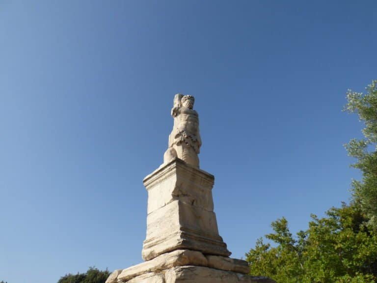 Ancient stone monument with a carved figure on top, set against a clear blue sky.