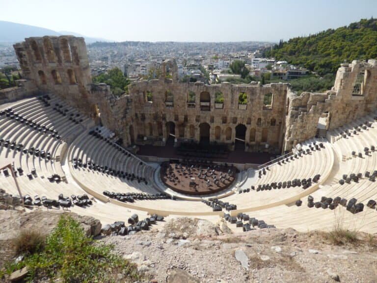 Ancient Greek theater with stone seating and stage, overlooking Athens cityscape.