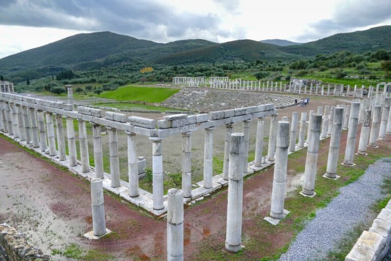 Ancient Greek ruins with columns and structures at Odyssey Academy, set against lush green hills and.