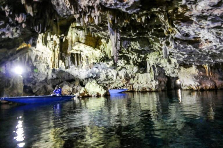 Kayakers exploring a illuminated cave interior on calm water.