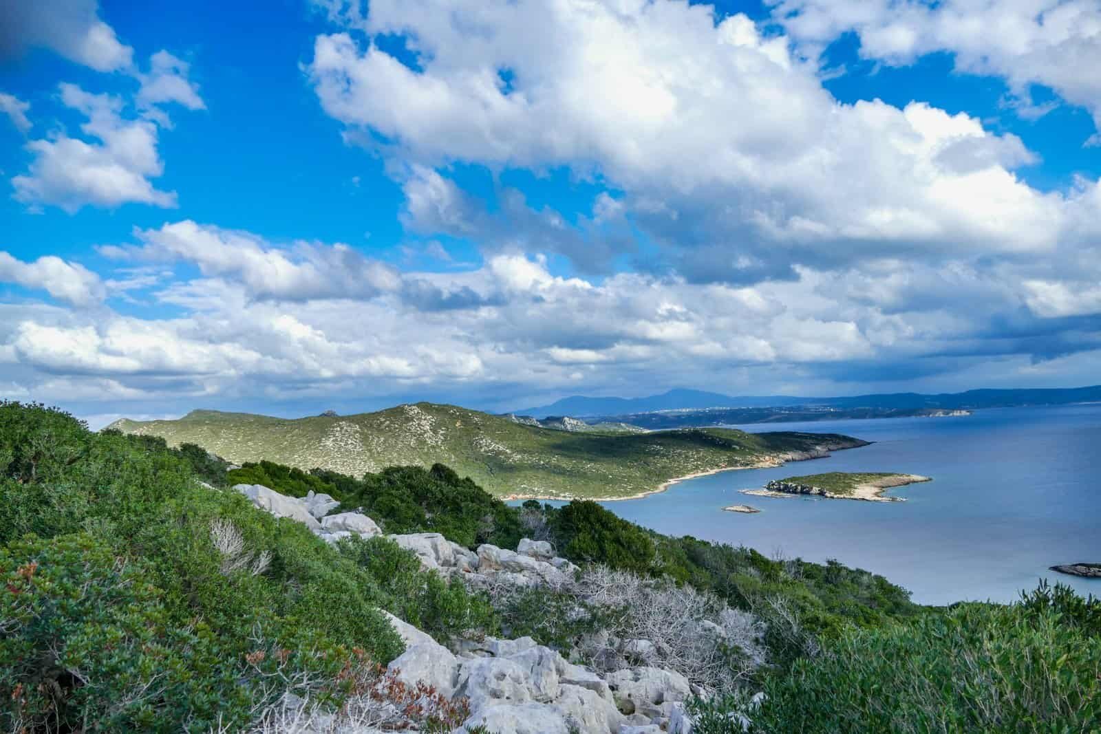 Beautiful coastal view featuring lush green hills, rocky terrain, and calm blue waters under a partl.