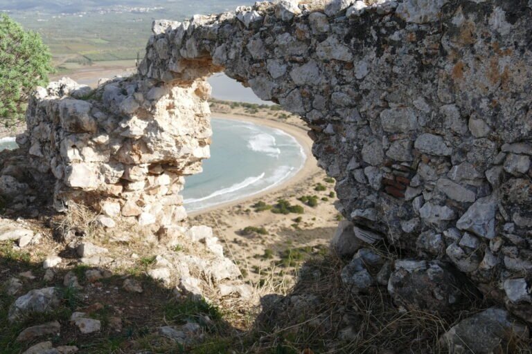 Ancient stone arch with a view of the beach and ocean in the background.