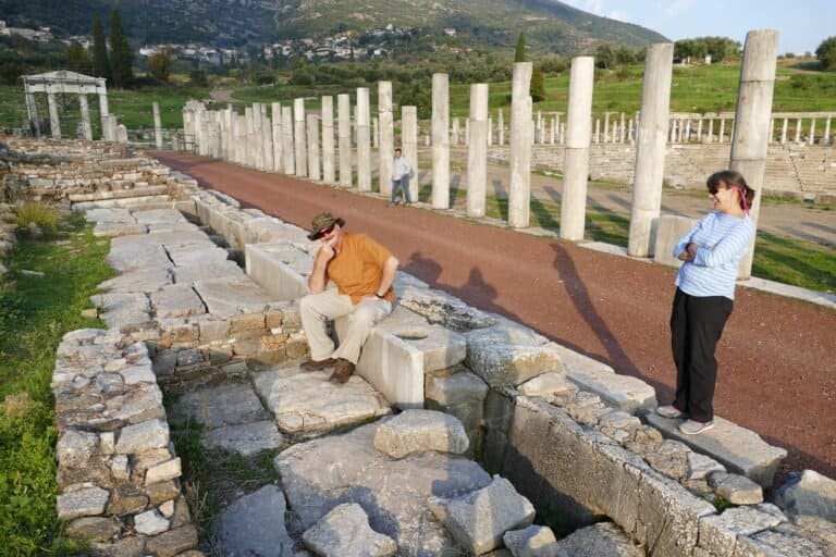 Tourists exploring ancient Greek ruins at Odyssey Academy site.
