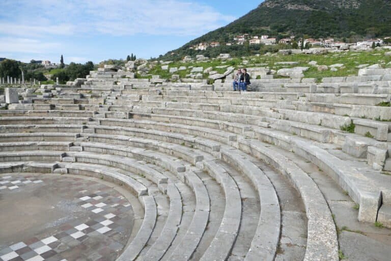 Historic Greek amphitheater with stone seating and scenic mountain backdrop.