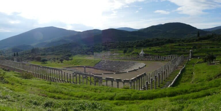 Scenic view of an ancient amphitheater surrounded by lush green hills and mountains.